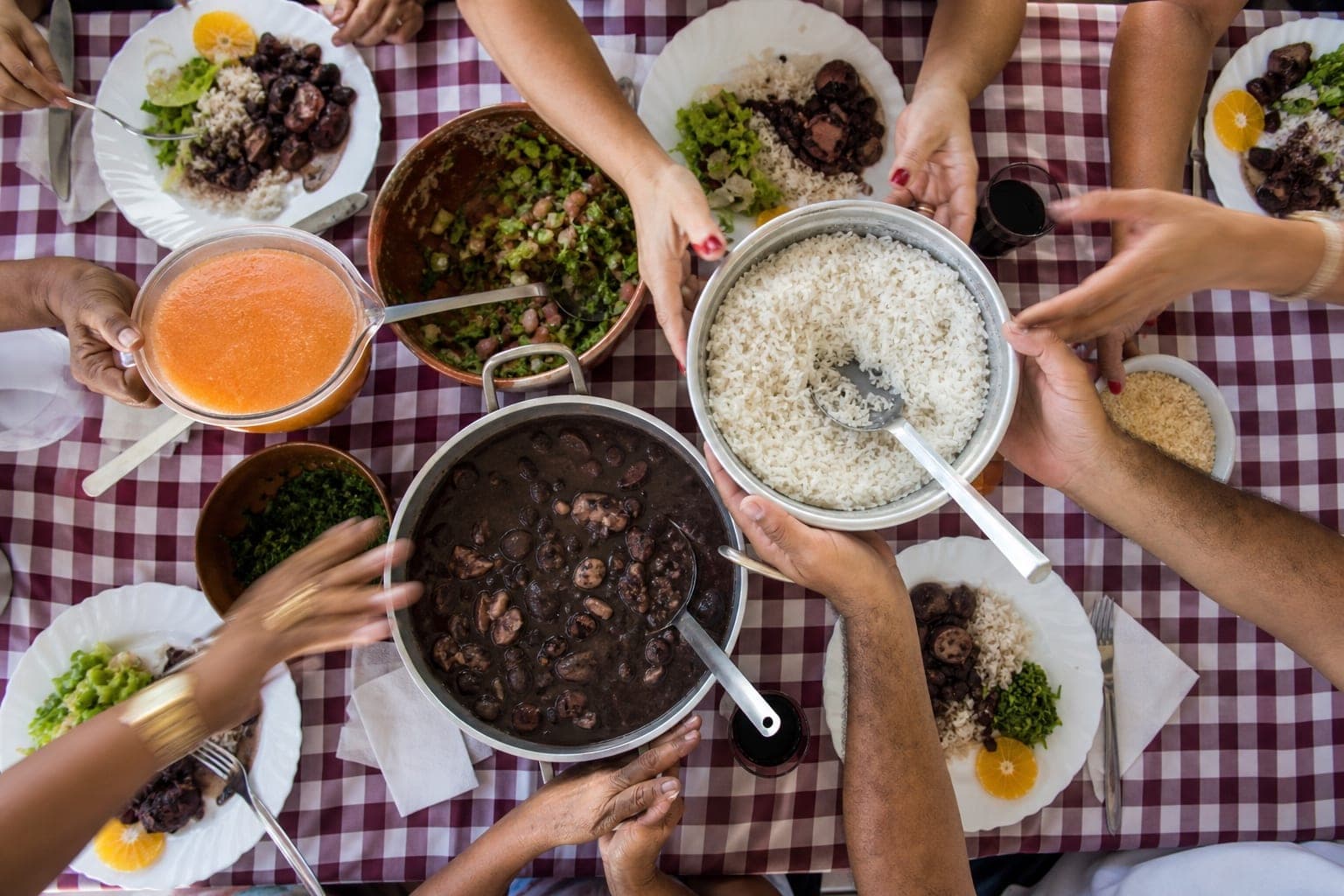 Mesa de almoço em família vista de cima, com mãos compartilhando os pratos