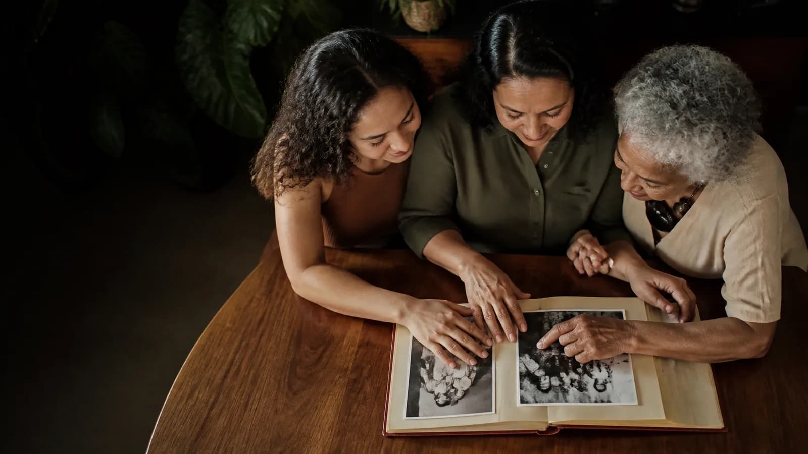 Mãos de três gerações reunidas sobre um álbum de família.